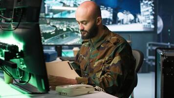 Military officer in command post receiving telephone call while looking at intel files. Intelligence specialist reading opponents strategy mission case file and talking on phone, camera A video