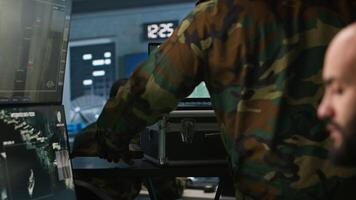 Military soldier wearing camo uniform in mission control center, overseeing national safety operations using laptop. Army expert examining data in monitoring room command center, camera A video
