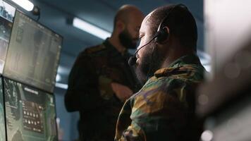 Military dispatcher using headphones microphone, offering information to commanders fighting on front lines. Army expert providing intel for troops in base of operations, camera A video