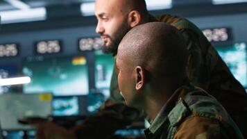 Army unit working in governmental facility next to colleague, operating surveillance monitoring tech with digital equipment. African american man doing job in base of operations, camera A video