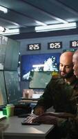 Vertical Air force officer and coworker talking while performing tactical level surveillance in command post. Teamworking military professionals using radar equipment to look at assault zones, camera B video