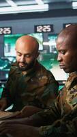 Vertical Army unit working in governmental facility next to coworker, doing brainstorming, operating surveillance tech. Team of soldiers doing job in HQ base of operations, camera B video