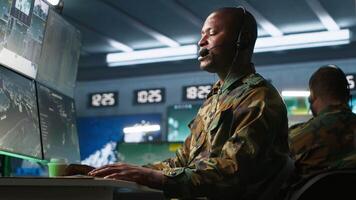 Army specialist working in war room operating surveillance tech, evaluating target data, talking in voice call. Dispatcher keeping in touch with allied troops engaging enemy forces, camera A video