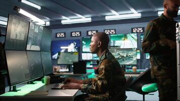 Intelligence operative in military base doing surveillance with digital radar equipment, operating missile systems. African american man monitoring army HQ CCTV for any unauthorized activity, camera B video