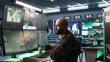 Man looking at screens in military HQ base housing operational missile defense system designed to intercept ballistic rockets. Special forces expert using tracking gear and radar systems, camera B video