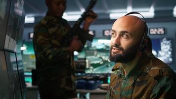 Middle Eastern military dispatcher relays info from army intelligence analysts to troops on front lines, close up. Radio communications operator discussing with colleague using headset mic, camera B video