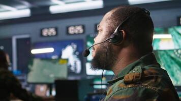 Military dispatcher using headphones microphone, offering information to commanders fighting on front lines. Army expert providing intel for troops in base of operations, camera B video