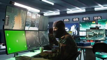 Masked intelligence corps agent overseeing national safety operations with mockup equipment. Special forces spy examining data in monitoring room with chroma key monitors, camera B video