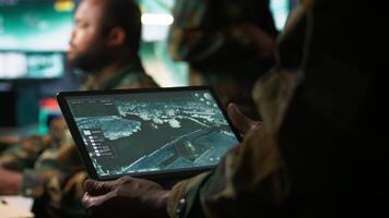 Army telecommunication systems operator using satellite software on tablet, providing combat support. Military dispatcher managing communications networks, with portable device, camera B video