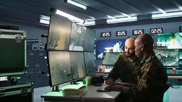 Air force officer and coworker talking while performing tactical level surveillance in command post. Teamworking military professionals using radar equipment to look at assault zones, camera B video