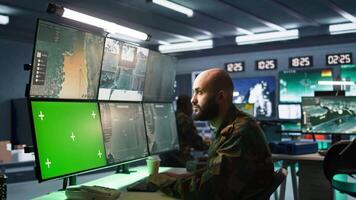 Army soldier looking at chroma key screens in command center housing operational missile defense system designed to intercept ballistic rockets. Specialist using mockup tracking gear, camera B video
