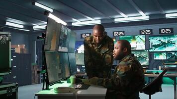 Military officers look at intel folder files on enemy battle formation, comparing with radar images. Army specialists looking at mission case file and equipment screens, camera B video