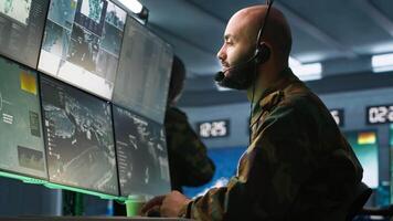 Military dispatcher using headphones microphone, offering info to infantry units fighting on front lines. Army expert providing intel for troops, coordinating mission activities, camera A video