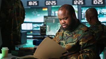 Military officer in command post receiving intel folder files on enemy battle formation. Intelligence specialist reading mission case file to collect data on opponents strategy, camera A video