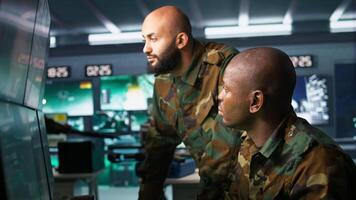 Army unit working in governmental facility next to colleague, operating surveillance monitoring tech with digital equipment. African american man doing job in base of operations, camera B video