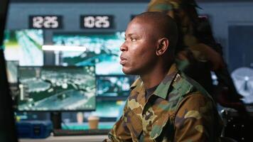 Intelligence operative in military base doing surveillance with digital radar equipment, operating missile systems. African american man monitoring army HQ CCTV for any unauthorized activity, camera A video