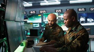 Army unit working in governmental facility next to coworker, doing brainstorming, operating surveillance tech. Team of soldiers doing job in HQ base of operations, camera B video