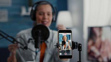 Famous internet influencer filming daily vlog with smartphone while telling life stories. Excited content creator sitting at home studio desk while broadcasting blog. Close up video