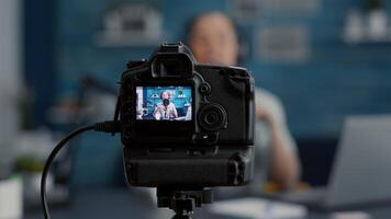 Modern camera filming influencer talking to audience. Popular social media content creator recording vlog for internet sharing platforms while sitting at studio desk. Close up video
