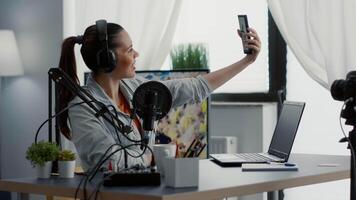 Famous internet influencer taking selfie photo with smartphone while streaming. Digital content creator sitting at home studio desk while taking pictures with touchscreen mobile phone. video