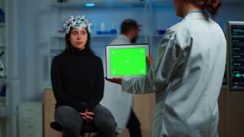 Neurologist doctor holding tablet with green screen in neurological research laboratory. Scientist using mockup chroma key display isolated desktop while patient with eeg headset wating in background video