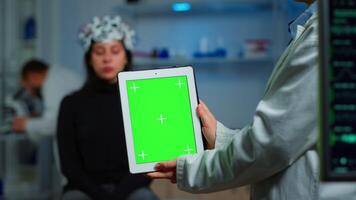 Health care researcher holding and looking at tablet with chroma key display in neurological lab. Team of scientists doing medical research reading on device with green screen, isolated mockup display video