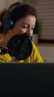 Vertical . Happy blogger reading messages of fans using smartphone sitting in home podcast studio during livestreaming, recording. Online show On-air production internet broadcast host streaming live content video