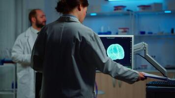 Researcher looking at monitor analysing brain scan while coworker discussing with patient in background about side effects, mind functions, nervous system, tomography scan working in laboratory video