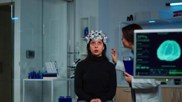 Neurological doctor cheking eeg headset explaining to patient diagnosis of disease and treatment for nervous system. Scientist researcher analysing brain scan and tomography on monitor in lab video