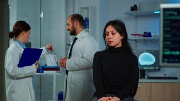 Team of scientists doctor discussing health status of patient, brain functions, nervous system, tomography scan while woman waiting for diagnosis of disease sitting in neurological research laboratory video