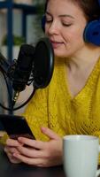 Vertical . blogger reading questions from fans using smartphone during livestreaming from home podcast studio. Show production broadcast presenter streaming live content recording digital media video