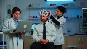 Medic in neuroscience working in neurological research laboratory developing brain experiment holding laptop explaning to man brainwave scanning headset side effects of nervous system treamtment. video