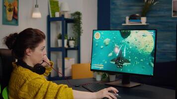 Focused woman gamer sitting on desk, putting on headset with a mic and starts playing game. Online streaming cyber performing on powerful personal computer during gaming tournament video