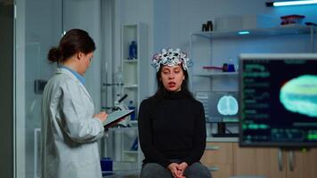 Researcher neurologist doctor asking patient's symptoms taking notes on tablet, adjusting high tech eeg headset. Doctor researcher controlling EEG headset analyzing brain functions and health status video