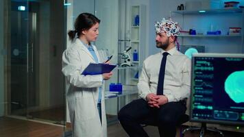 Medical doctor talking about symptoms of disease during investigations using high tech brainwave scanning headset. Researcher analysing health status of man patient, brain functions, nervous system. video