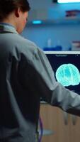Vertical . Researcher looking at monitor analysing brain scan while coworker discussing with patient in background about side effects, mind functions, nervous system, tomography scan working in laboratory video