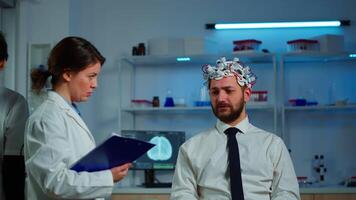 Researcher neurologist doctor asking man's symptoms taking notes on clipboard before brain scan with brainwave scanning headset. Scientist analyzing health status, nervous system, tomography scan video