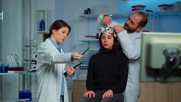 Professional neurological researcher explaning treatment result pointing on monitor while medical scientist adjusting eeg headset preparing for brain scan analysing electrical activity, nervous system video