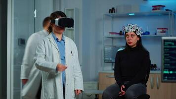Professional researcher wearing virtual reality glasses using medical inovation in lab analysing brain scan of patient. Team of neurological doctors working with equipment high tech simulator device video