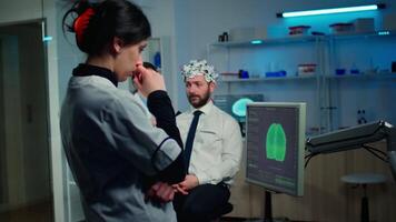 Woman researcher looking at monitor analysing brain scan while coworker discussing with patient in background about side effects, mind functions, nervous system, tomography scan working in laboratory video