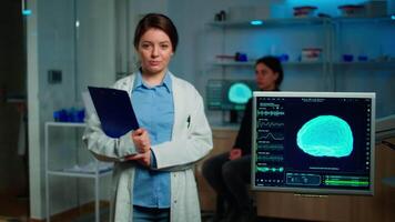 Portrait of medical neurologist researcher looking at camera smiling holding clipdoard while coworker discussing with patient about brain health care, nervous system, tomography scan working in lab video