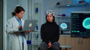 Specialist neurologist doctor taking notes on laptop asking patient's symptoms adjusting high tech eeg headset. Doctor researcher controlling EEG headset analyzing brain functions and health status video