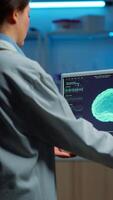 Vertical . Neurologist doctor reading informations of patient looking at monitor analysing brain scan discussing with patient wearing eeg headset. Scientist taking notes examining nervous system of woman in lab video