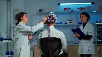 Man patient wearing performant eeg headset scanning brain electrical activity in neurological research laboratory while medical researcher controlling it, examining nervous system, nurse taking notes video