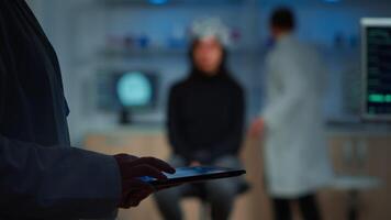 Close up of expert scientist in neurological dysfunctions standing in laboratory working at tablet. Medical researcher preparing patient for brain scan analysing electrical activity of nervous system video