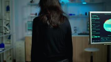 Stressed patient sitting on chair in neurological laboratory waiting for medical researcher investigating brain functions using high tech and neurology tools. Nervous system scan showing on monitor video