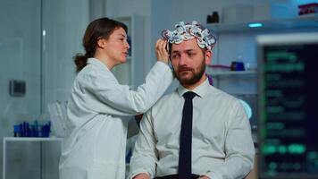 Patient with brainwave scanning headset sitting in brain study laboratory while neurologist scientist adjusting high tech device. Man visiting professional doctor treating nervous system dysfunctions video