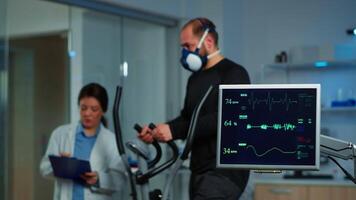 Team of medial researchers monitoring vo2 of man performance sports wearing mask running. Lab science doctor measuring endurance of sportsman while ekg scan runs on computer screen in laboratory video