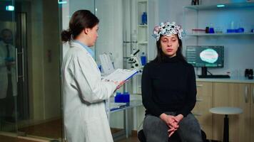 Neurologist doctor asking symptoms of patient taking notes on clipboard, adjusting high tech brain scanner. Medical scientist controlling EEG headset analyzing brain functions and health status video
