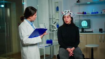 Medical doctor and patient discussing about symptoms of disease during eeg scan using high tech headset in lab. Analysing health status of woman, brain functions, nervous system, digital tomography video